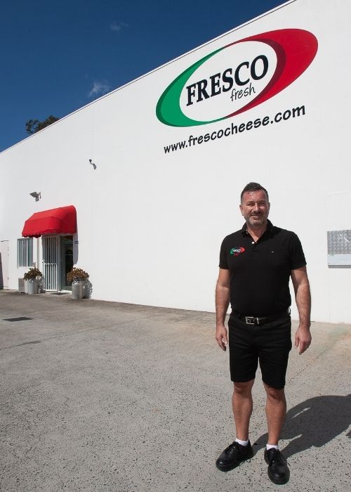 Man in shorts standing in front of the Fresco Cheese building | featured image for Contact Us.