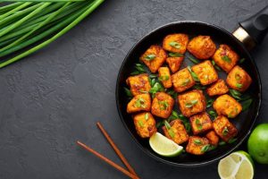 Grilled Paneer in a frying pan with limes next to the pan | featured image for Home.